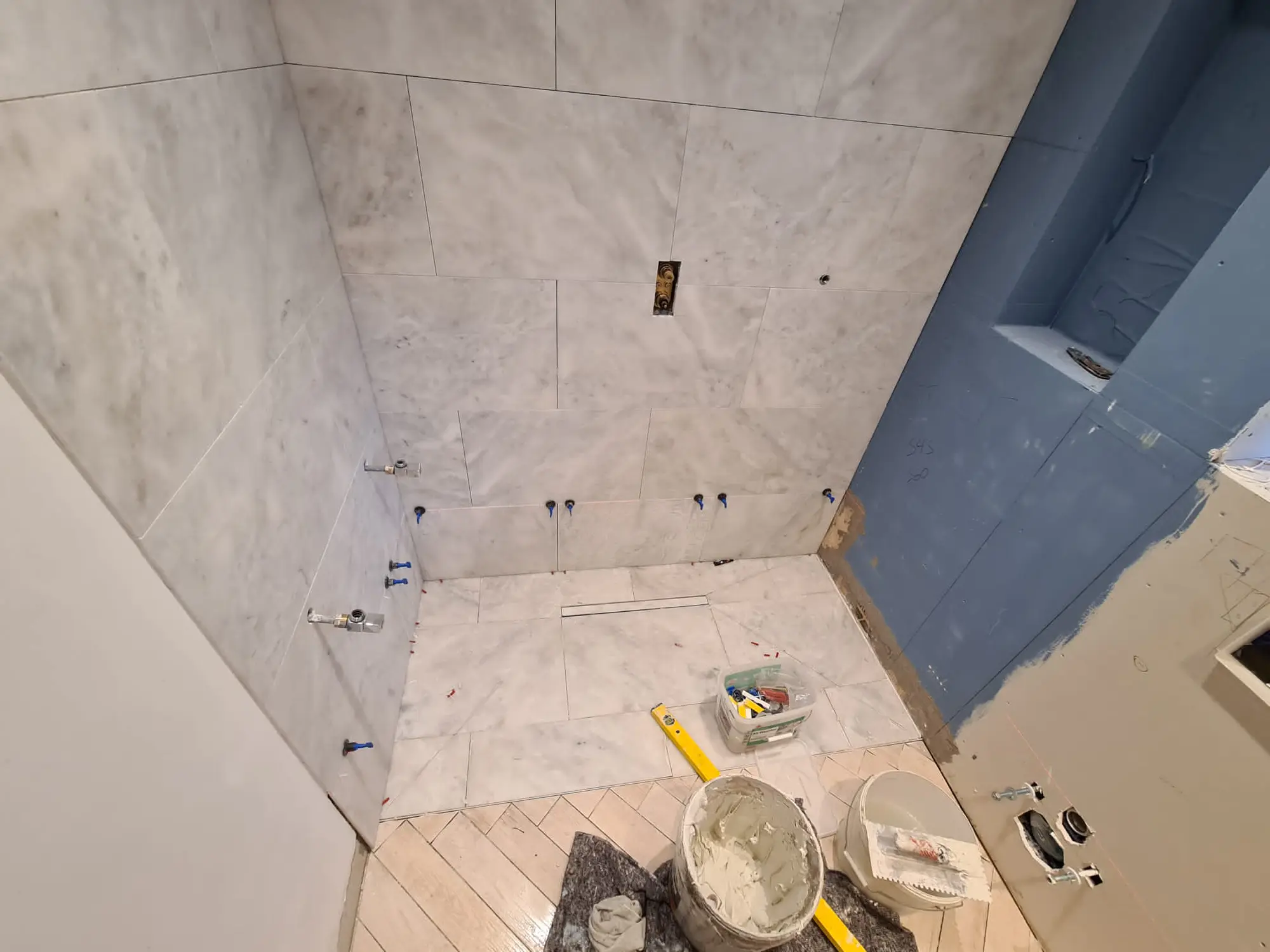 Pale marble-effect wet room tiling in progress over blue backer board