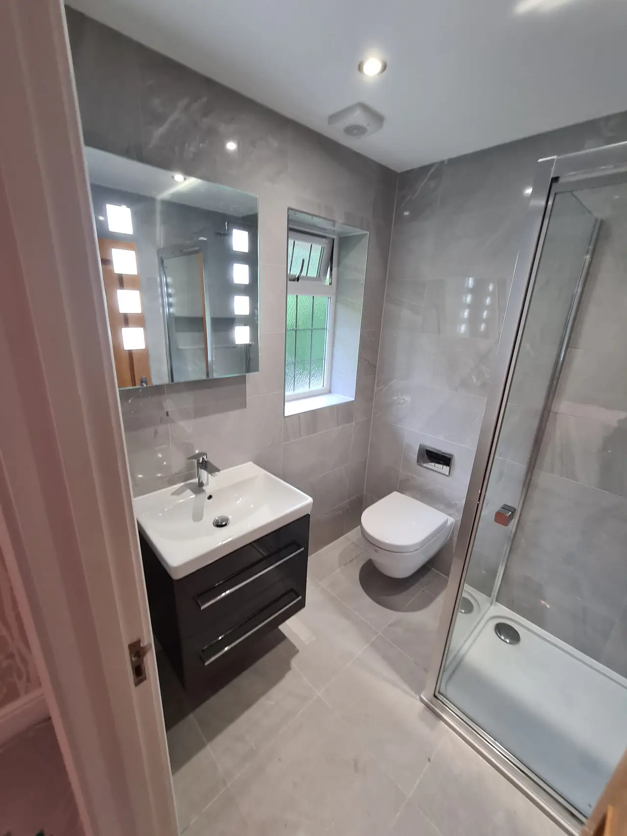 Finished grey shower room with a dark vanity and glazed corner enclosure
