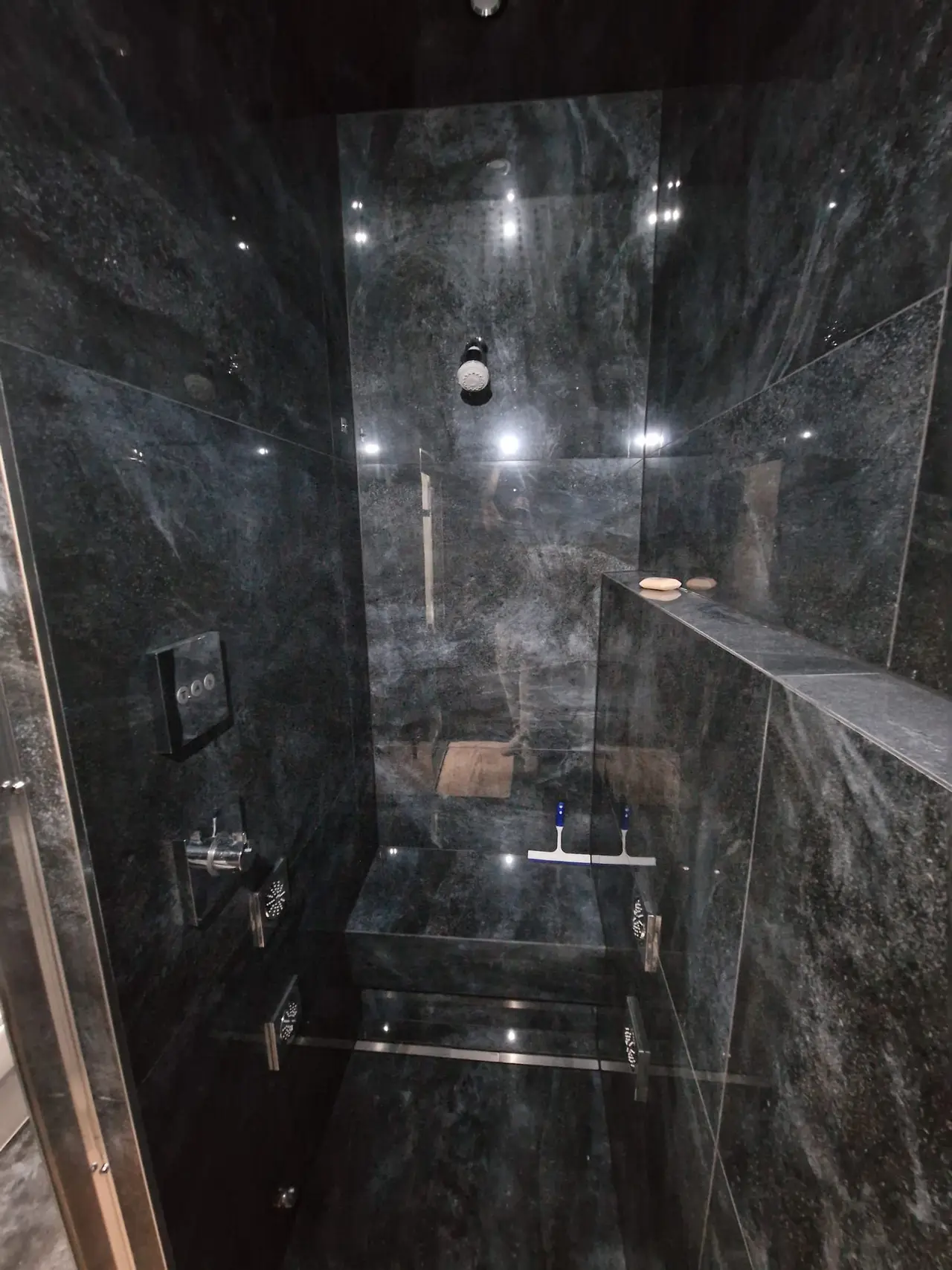 Polished dark stone walk-in shower with a built-in bench and glass door