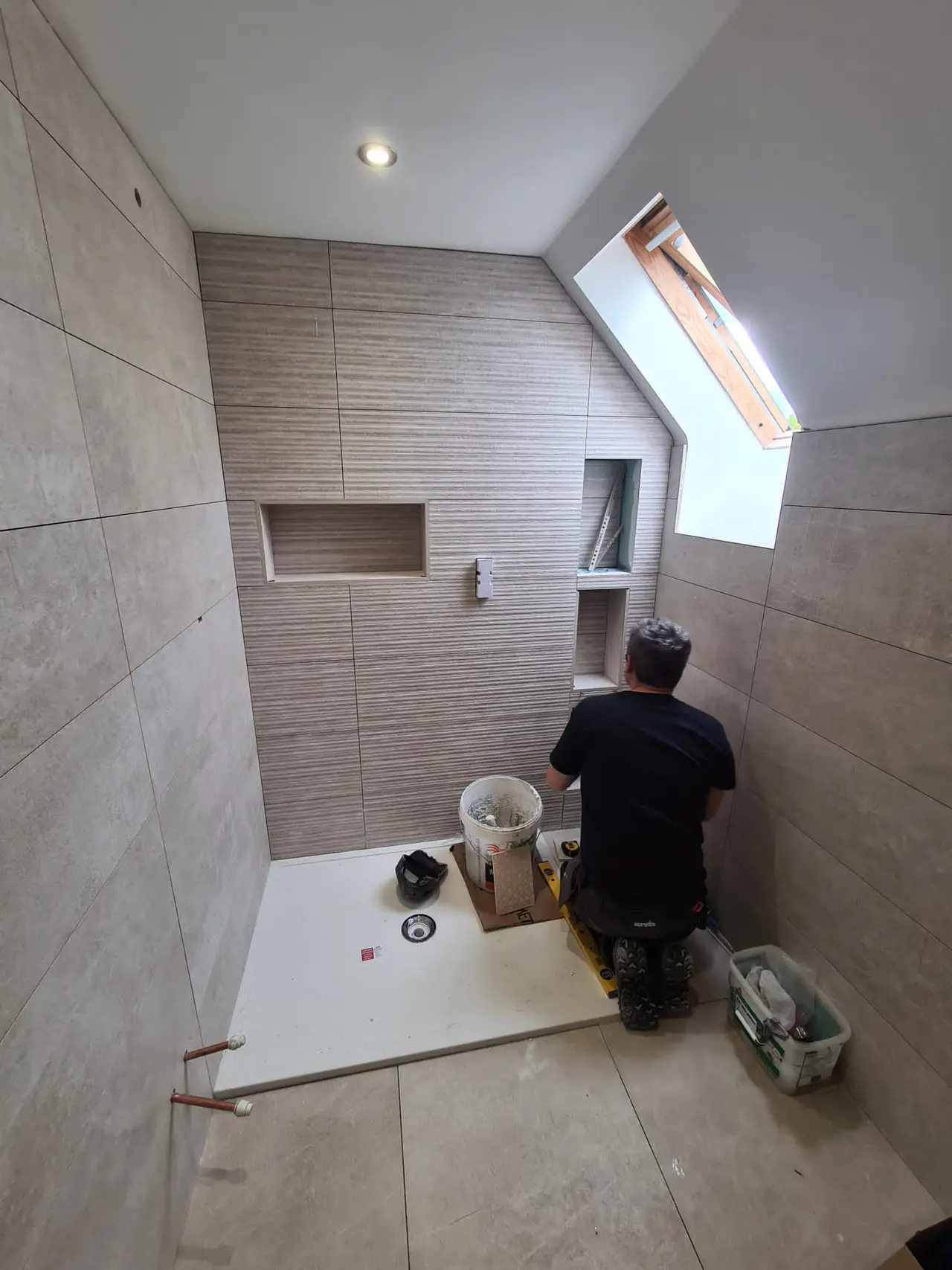 Striped feature tiles and recessed shelves being fitted in a loft shower