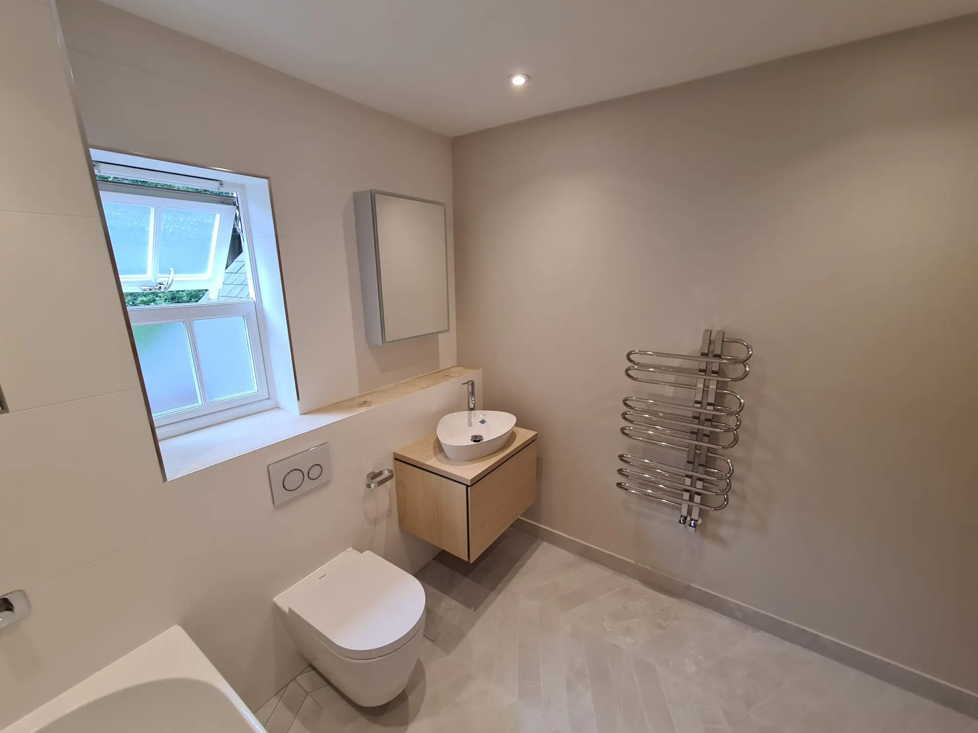 Light bathroom with a vessel basin, wall-hung toilet and chrome towel rail