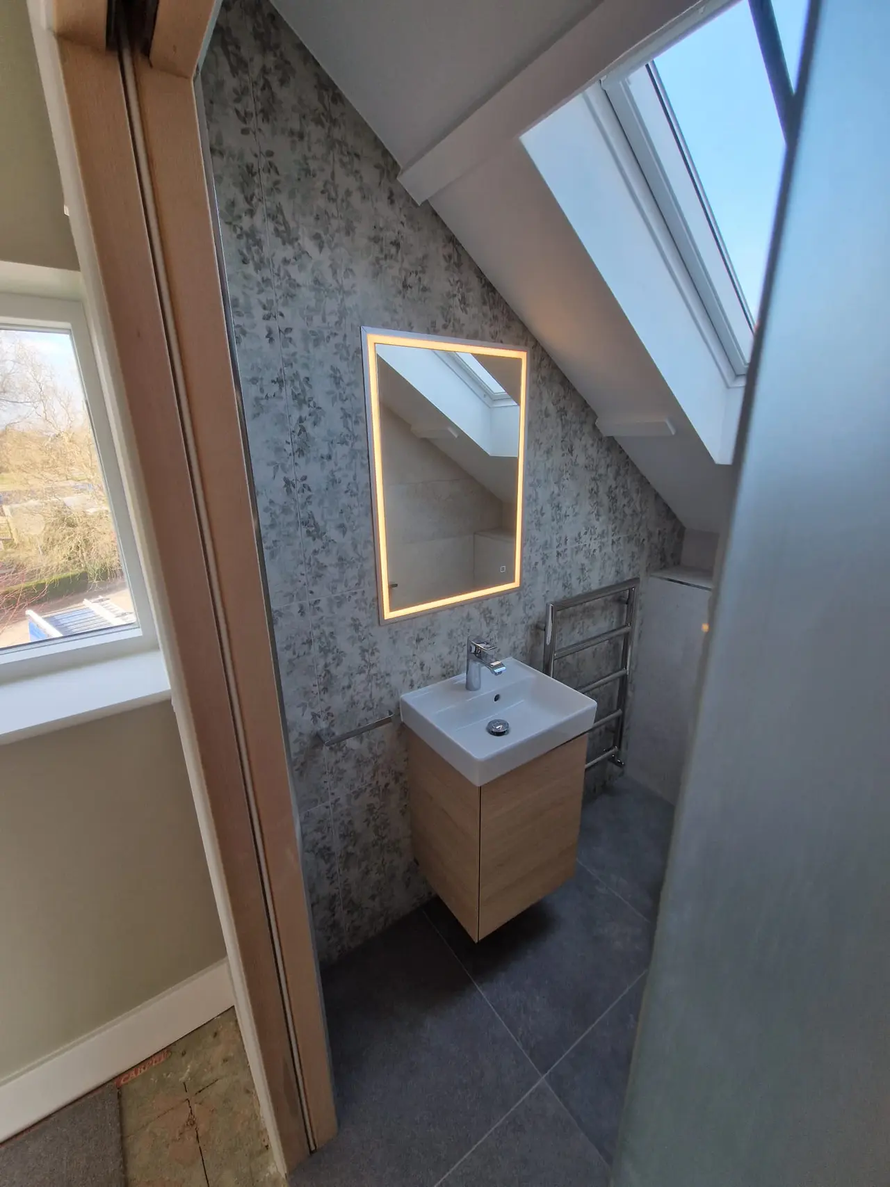 Finished loft ensuite with a floral feature wall and illuminated mirror
