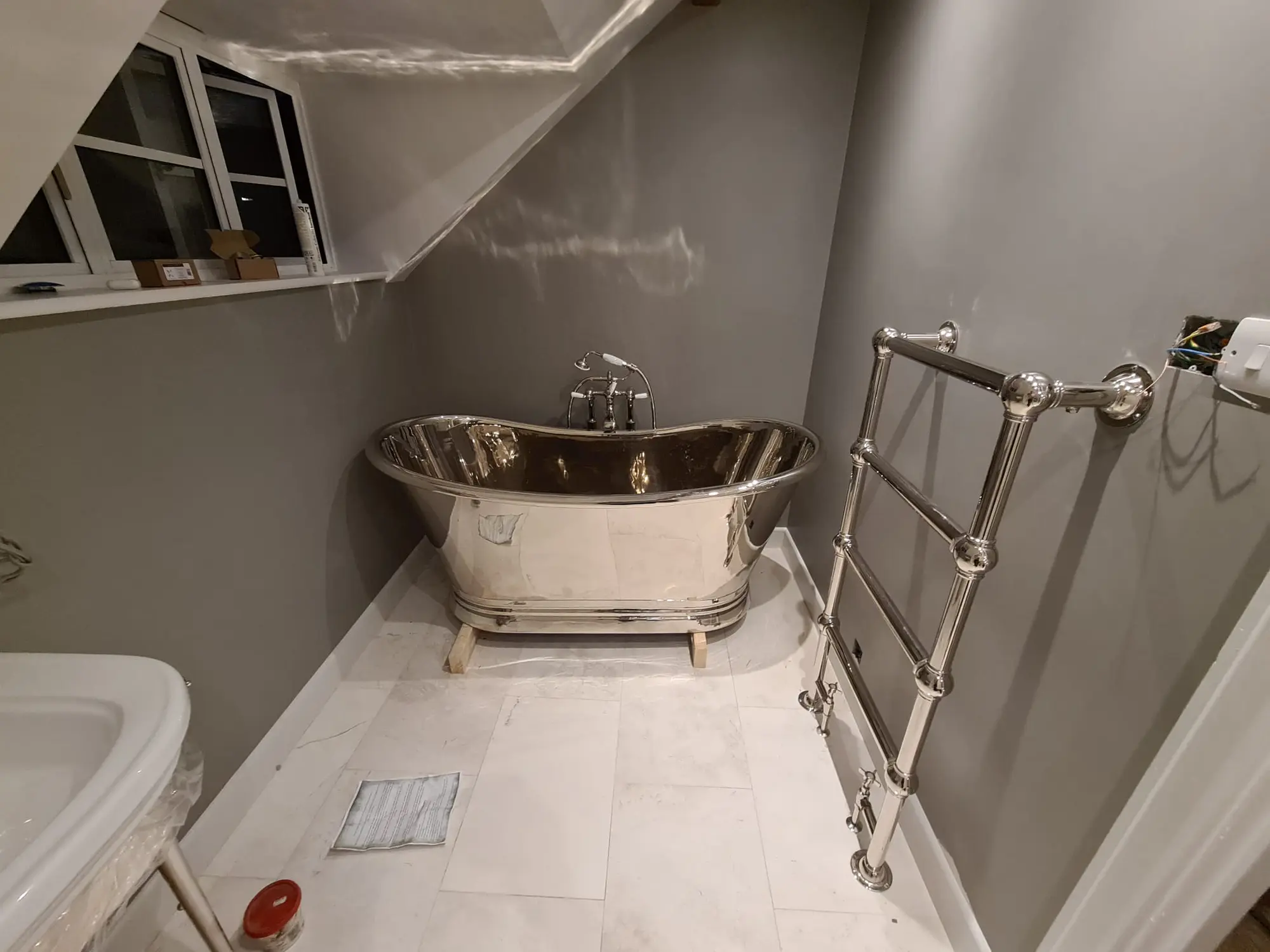 Polished metal roll-top bath beneath a sloping ceiling