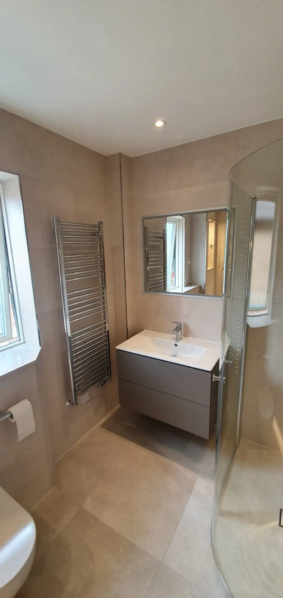 Beige bathroom with a curved shower enclosure and floating grey vanity