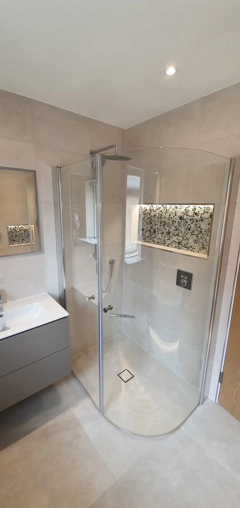 Curved shower enclosure beside a pebble-lined recessed shelf