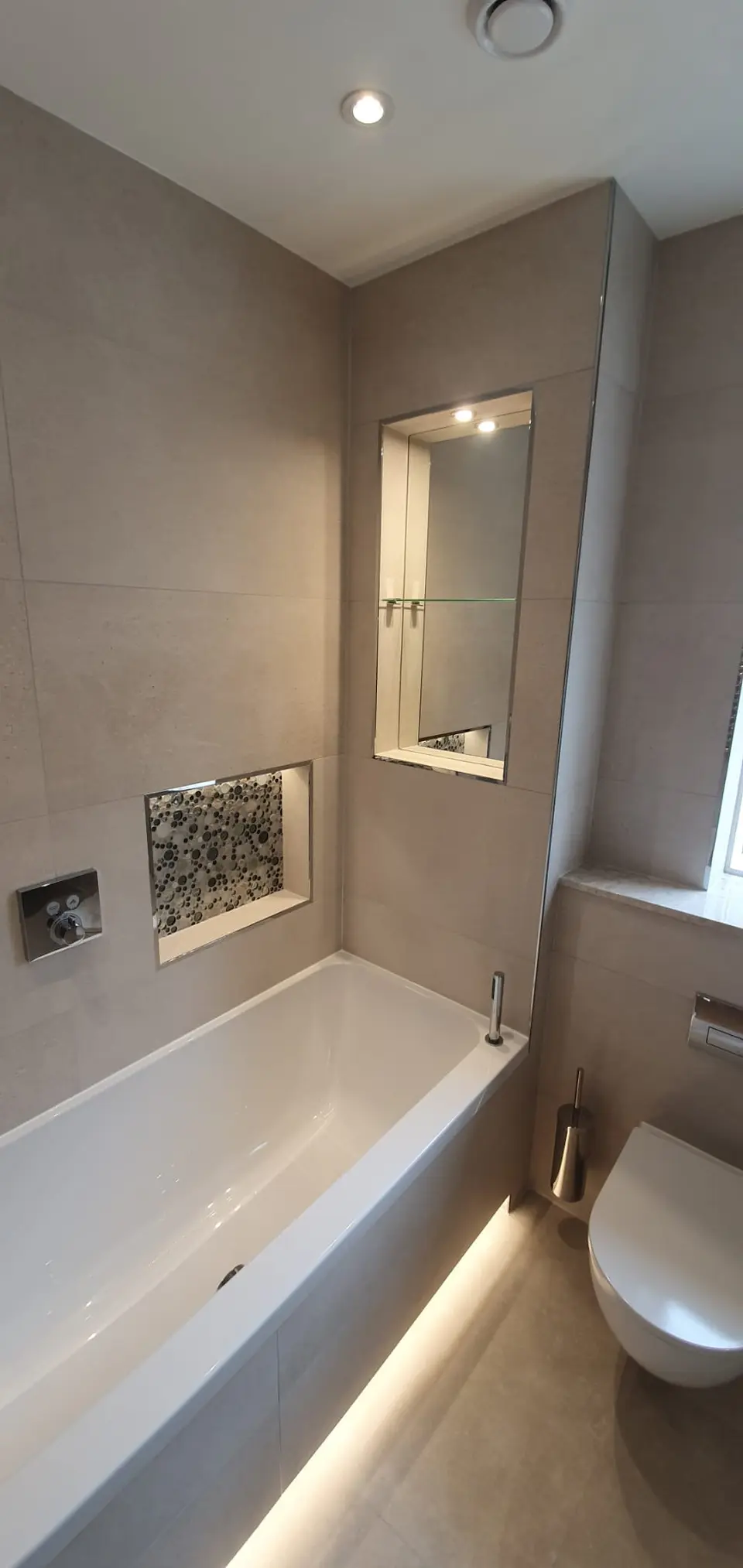 Recessed bath with an illuminated mirrored cabinet and pebble-lined niche