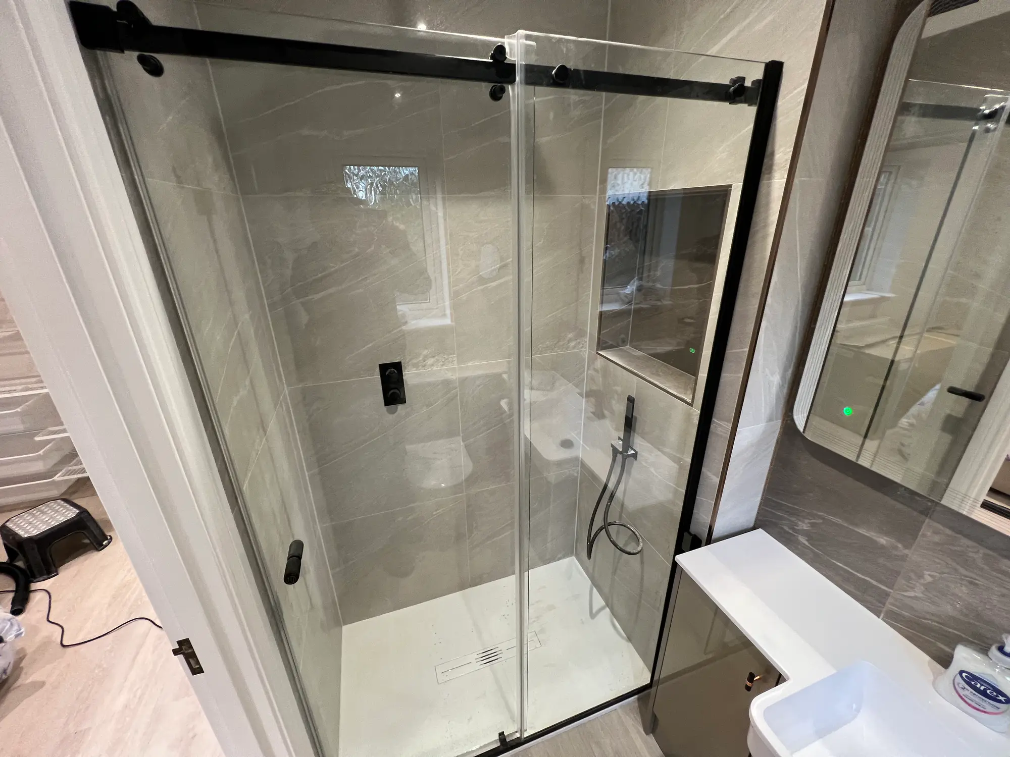 Glass shower enclosure with black fittings in a light stone bathroom