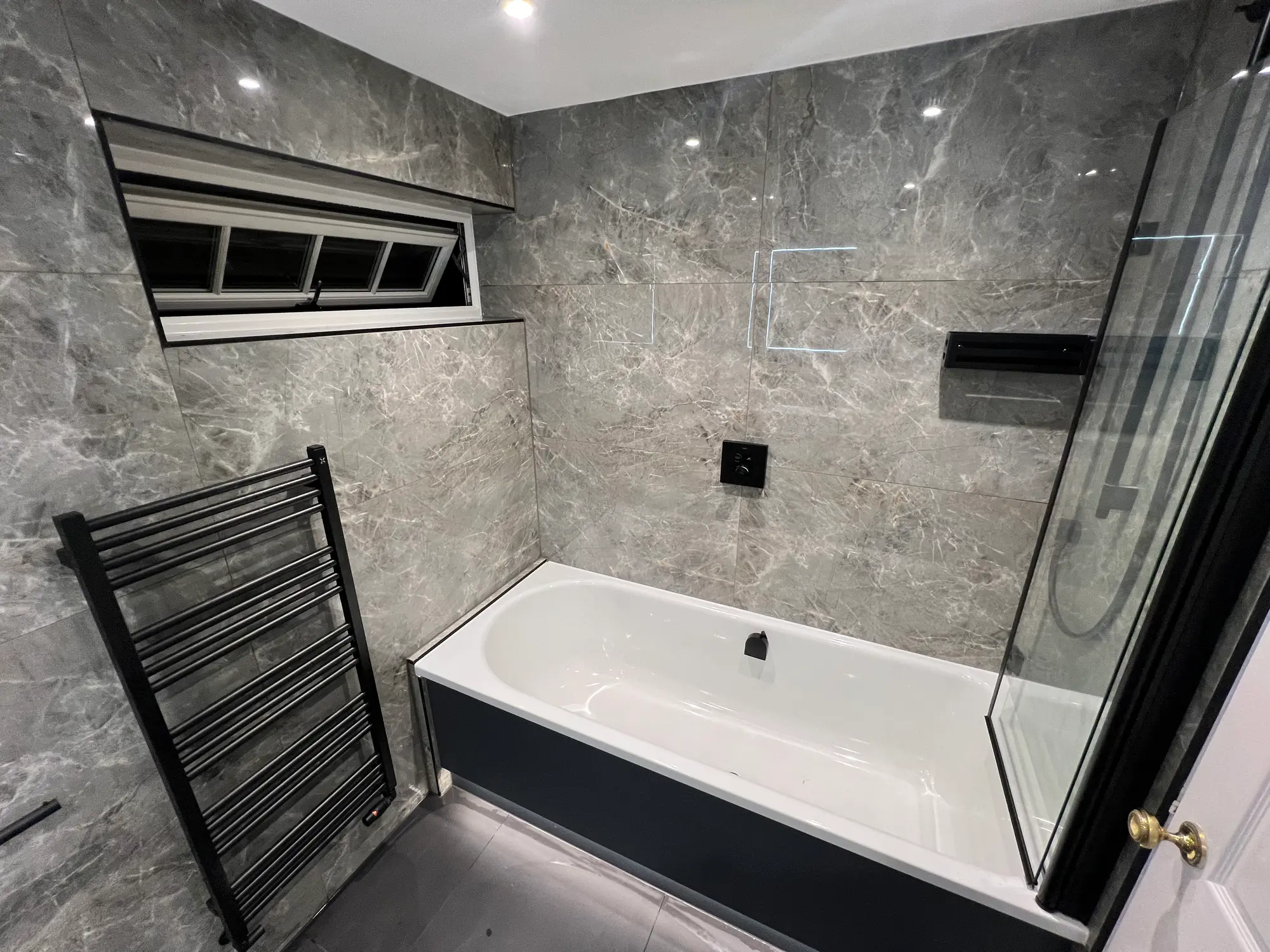 Grey marble bathroom with a dark panelled bath and black towel rail