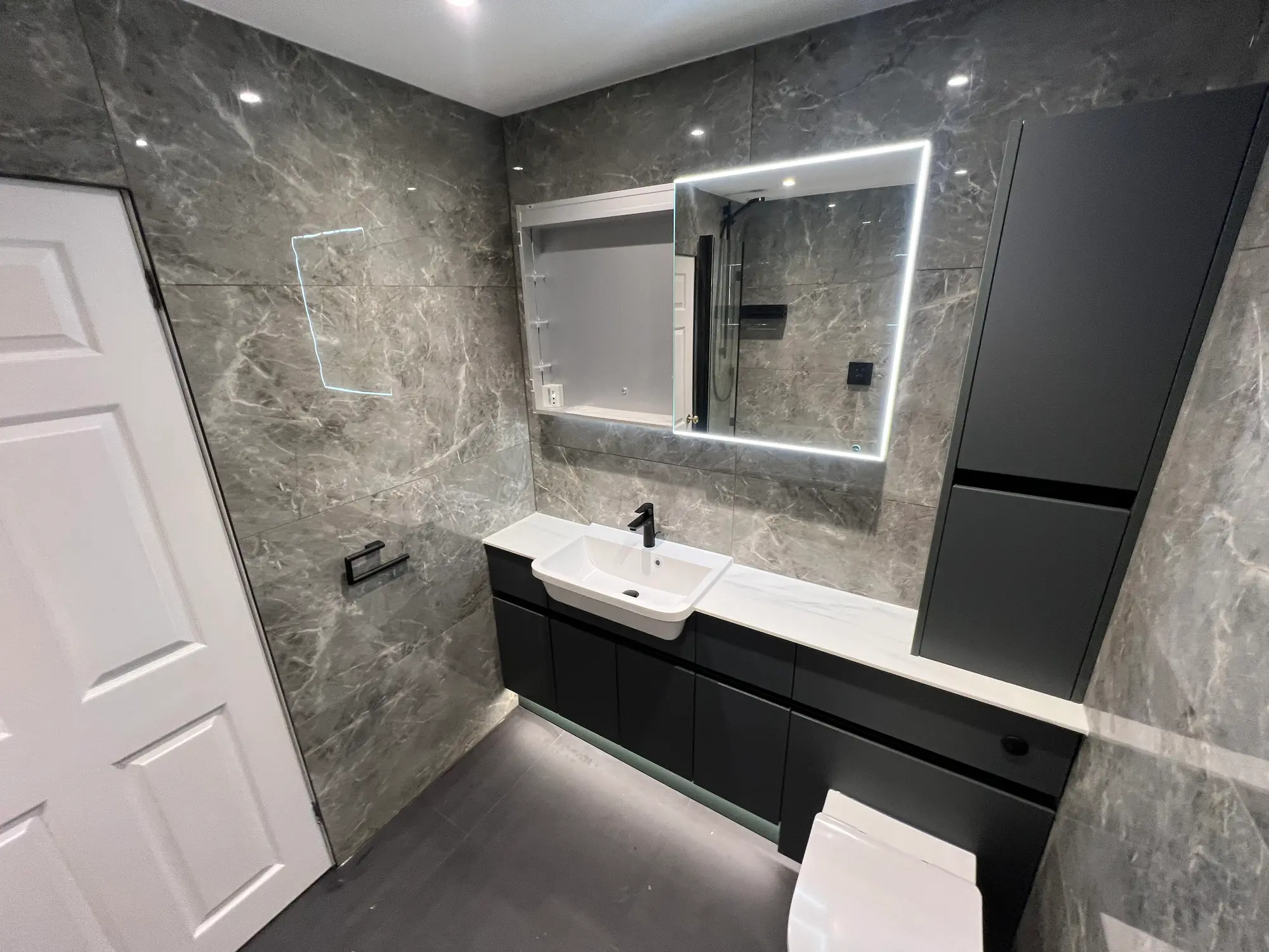 Grey marble vanity wall with black cabinetry and an illuminated mirror