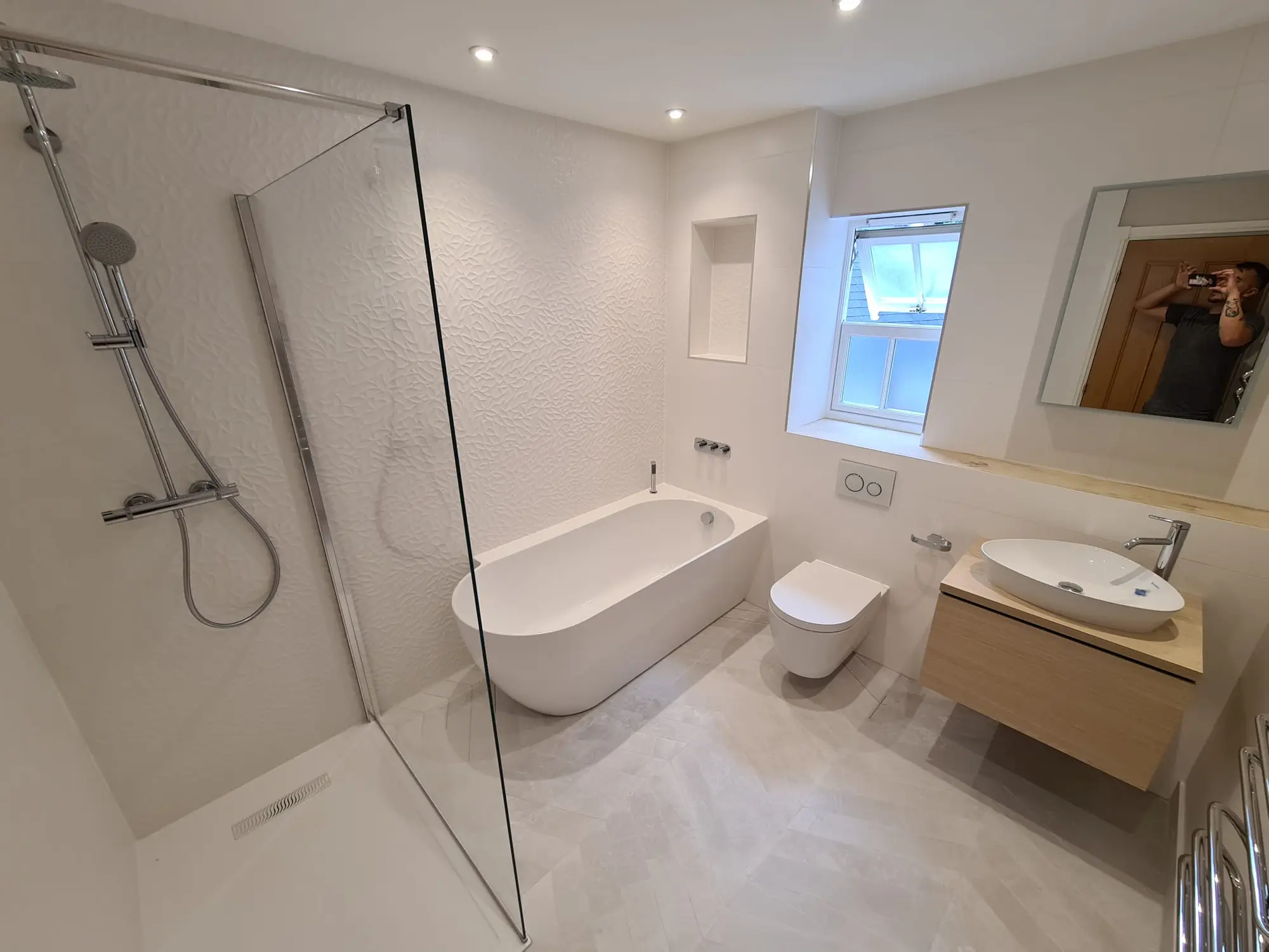 White bathroom with a freestanding bath, open shower and textured wall tiles